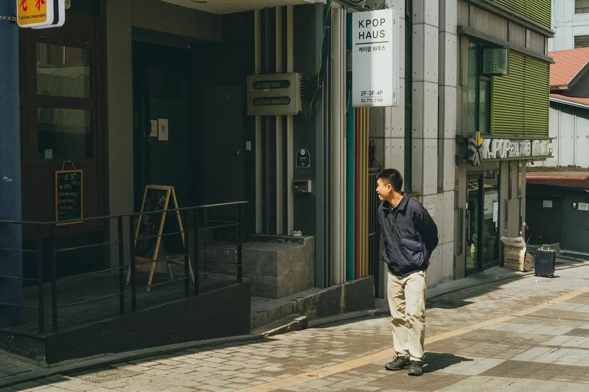 서울 도심의 K-POP 주제 건물 뒤에서 남자가 걷고 있는 장면.
