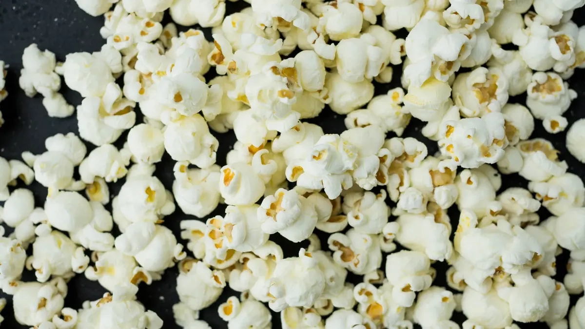 A close-up view of freshly popped popcorn scattered on a dark surface, ideal as a snack.